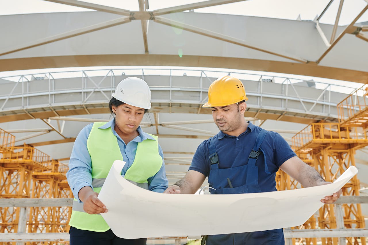 About Male and female engineers discussing blueprints at a construction site, promoting teamwork and planning.