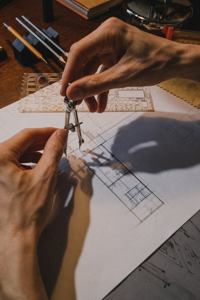 Home Detailed shot of hands using a compass on an architectural blueprint with drafting tools.